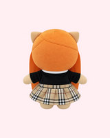 Back view of Ice Spice Hello Kitty plush showing long orange hair, a black top and a beige plaid skirt on a pale pink background.