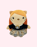 Front view of Ice Spice Hello Kitty plush with orange hair, a black top and a beige plaid skirt on a pale pink background.
