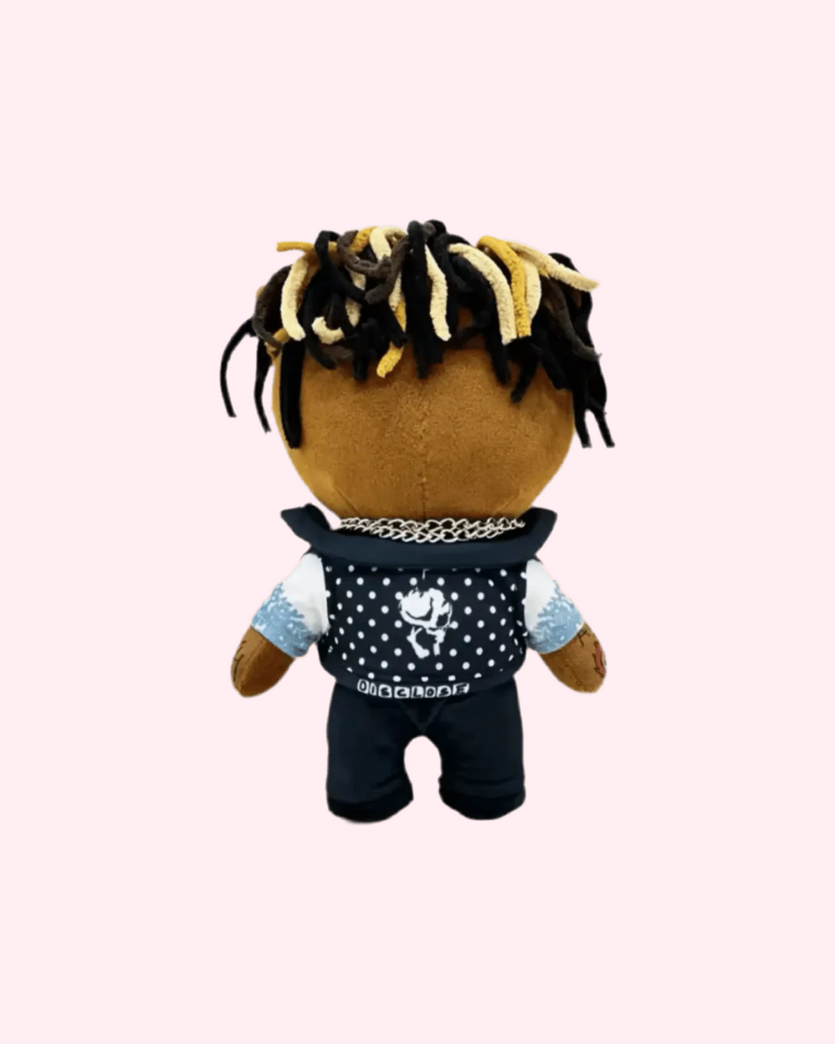 Back view of Juice WRLD Hello Kitty plush with black-and-blond yarn dreadlocks, a silver chain, a black patterned vest and black trousers, on a pale pink background.