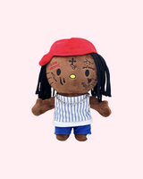 Front view of Lil Wayne Hello Kitty plush with a red cap, black yarn hair, striped top and blue shorts on a pale pink background.