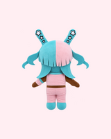 Back view of Megan Thee Stallion Hello Kitty plush showing cyan hair, pink clothing and cyan boots on a pale pink background.
