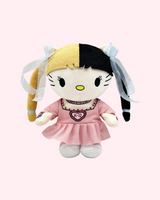 Front view of Melanie Martinez Hello Kitty plush with blond-and-black pigtails, a pink dress and white shoes, on a pale pink background.
