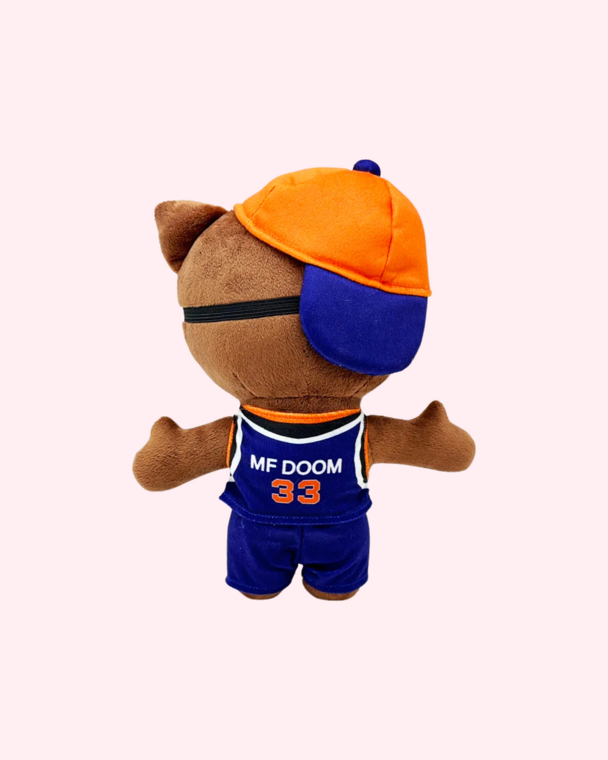 Back view of MF DOOM Hello Kitty plush with an orange-and-blue cap and a blue basketball outfit with MF DOOM and number 33 on the back, on a pale pink background.