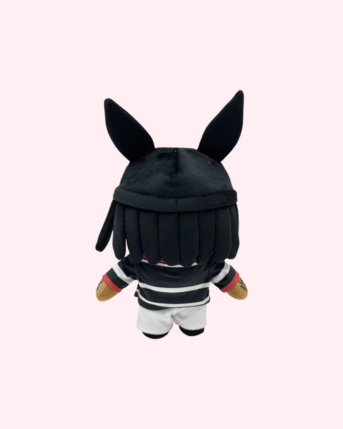 Back view of Playboi Carti Hello Kitty plush with a black hat with tall ears, dark braids and a black-and-white printed outfit, on a pale pink background.