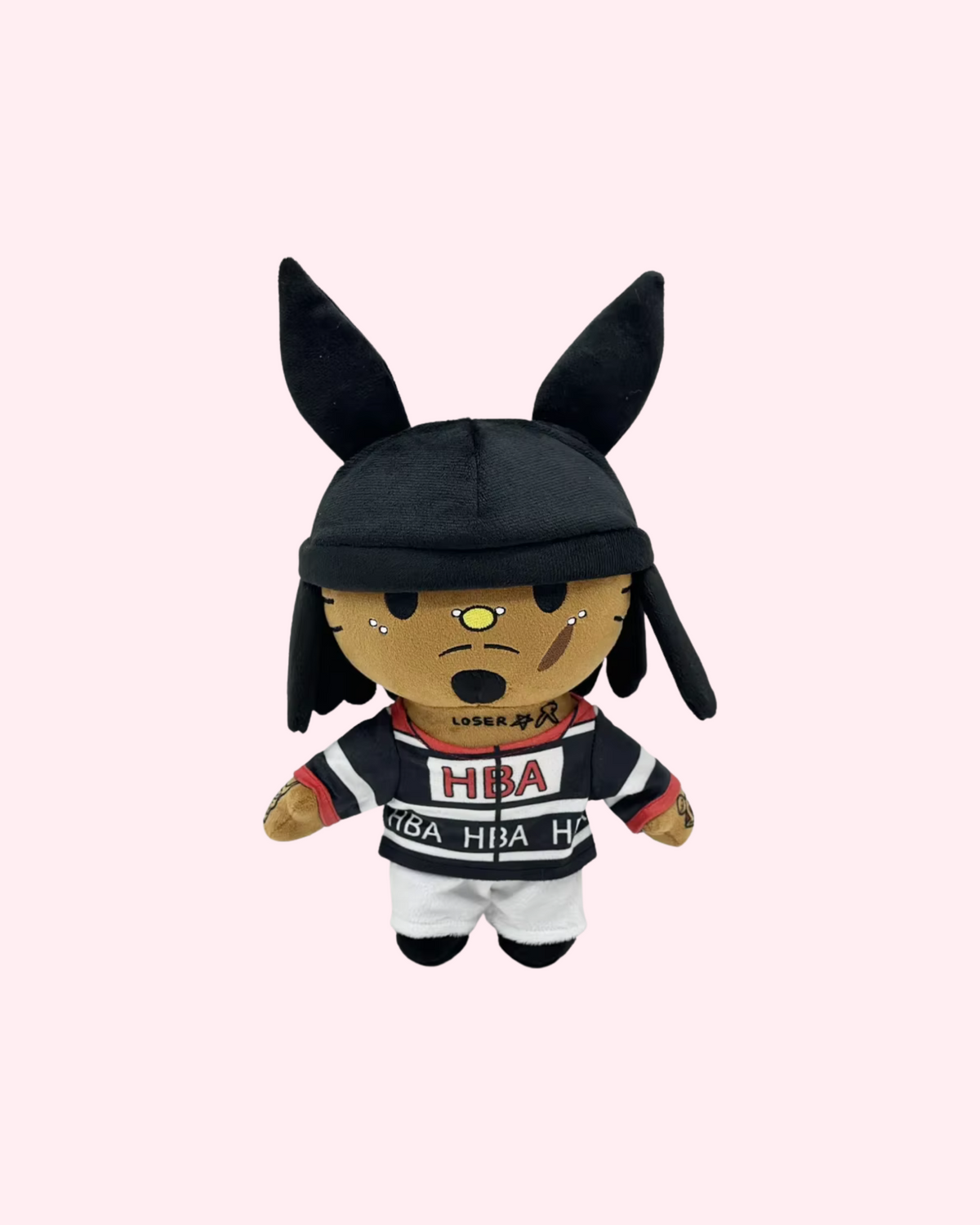 Front view of Playboi Carti Hello Kitty plush with a black hat with tall ears, dark braids and a black-and-white printed outfit, on a pale pink background.