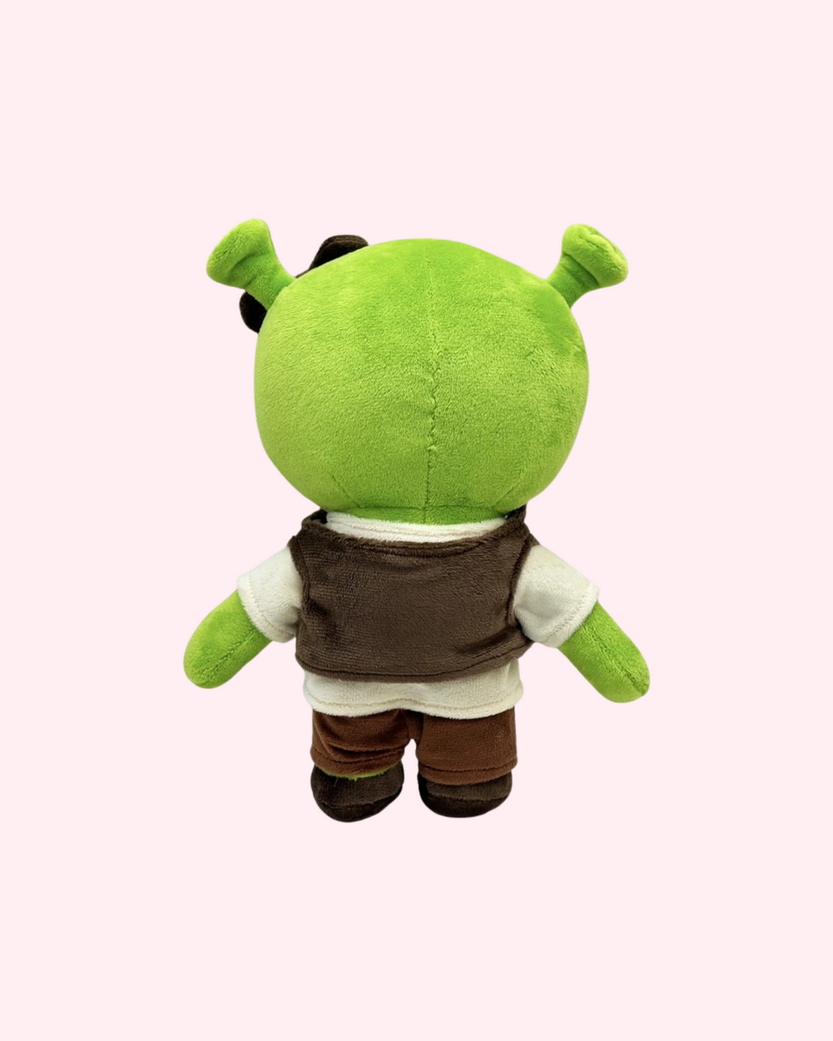Back view of Shrek Hello Kitty plush with green ogre ears, a brown vest over a cream tunic and brown trousers, on a pale pink background.