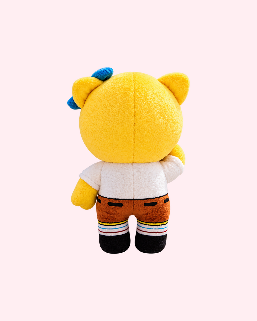Back view of SpongeBob Hello Kitty plush with yellow fabric, a blue bow, a white shirt, brown shorts and striped socks, on a pale pink background.