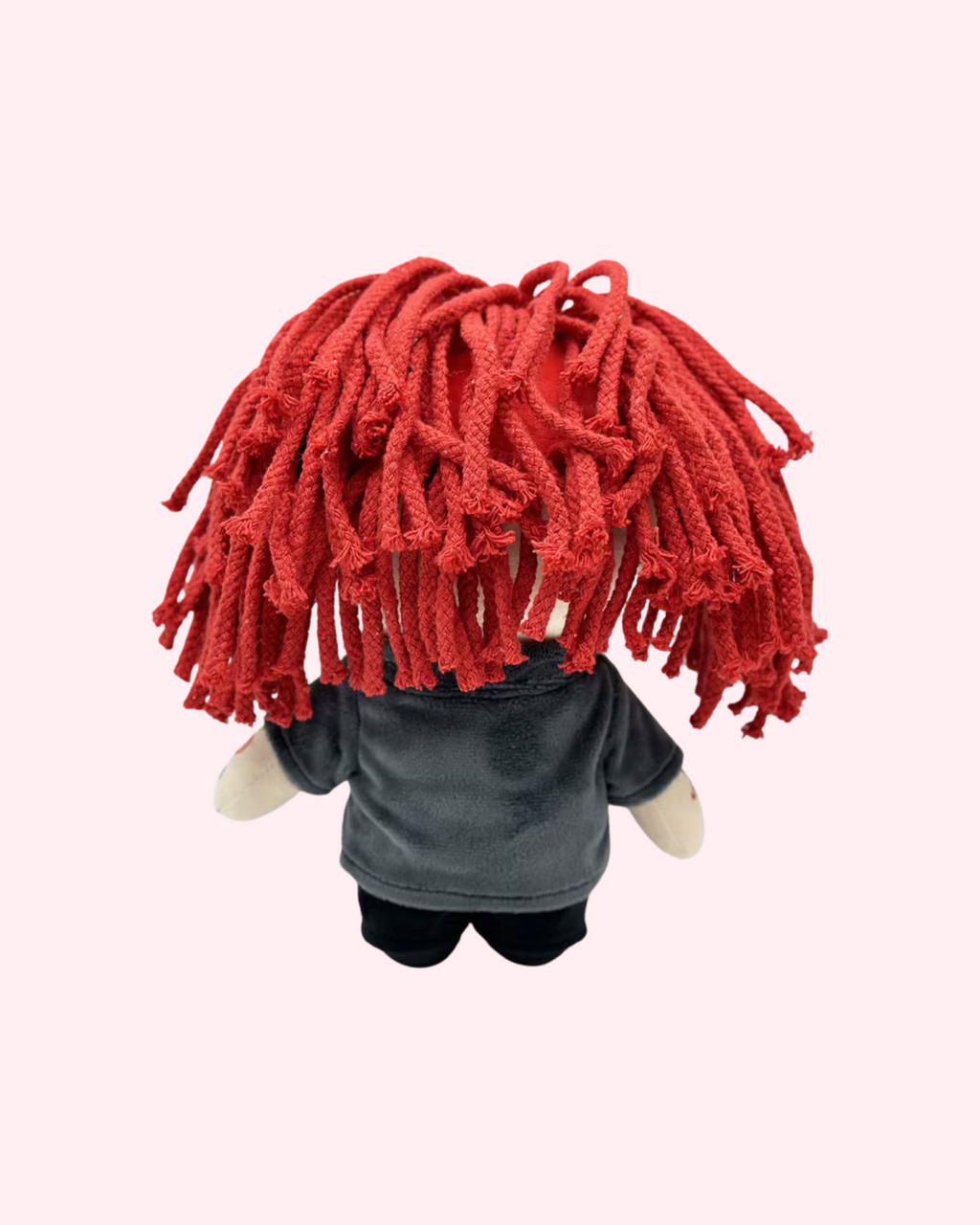 Back view of Trippie Redd Hello Kitty plush showing red yarn hair and dark clothes on a pale pink background.