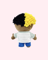 Back view of XXXTentacion Hello Kitty plush with yellow-and-black hair, a white shirt and blue shorts, on a pale pink background.